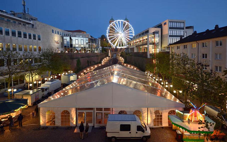 A Ferris wheel is shown in the background of a large festival tent in a square.