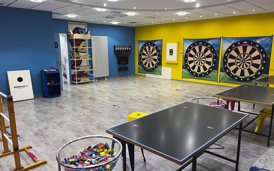 A spacious room holds dart boards, ping pong tables, and other game equipment.