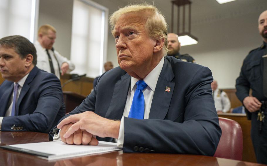 Donald Trump sits at a table in a courtroom with his hands folded in front of him.