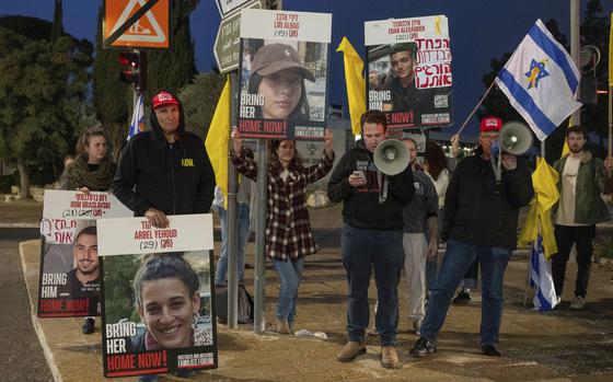 Israeli citizens hold up posters with photos of hostages held in Gaza during a demonstration on a street corner.