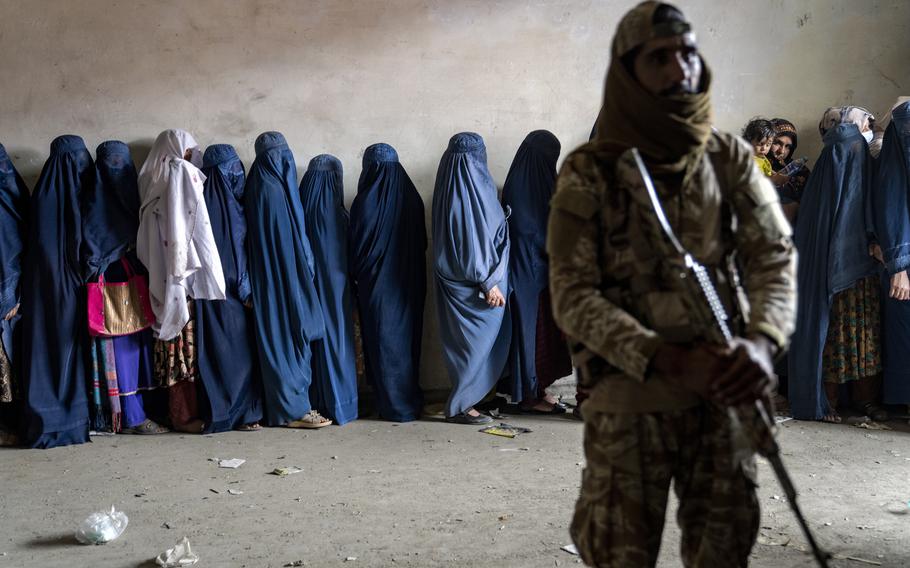 A Taliban fighter stands guard as women wait to receive food rations.