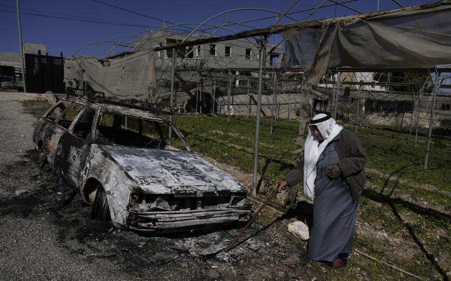 A Palestinian stands beside a torched car.