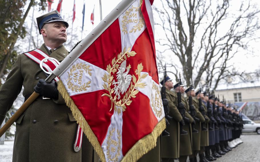 Polish soldiers stand in formation with one holding a a flag.