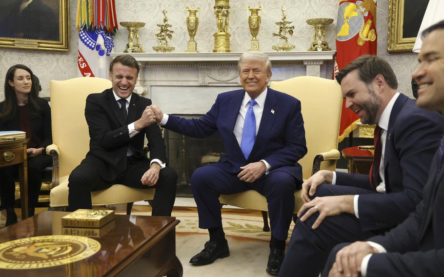 Emmanuel Macron and Donald Trump grin while gripping each other’s hands while seated.