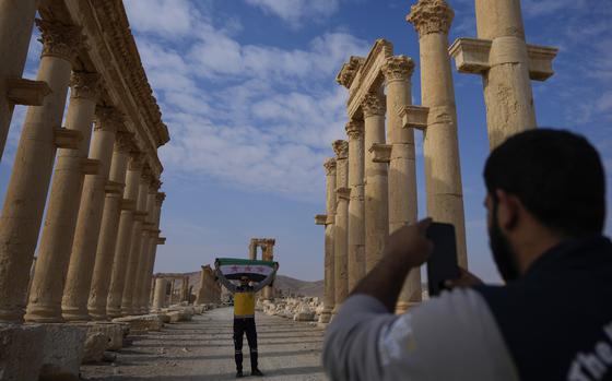 A member of the Syrian Civil Defense takes a photo of his colleague holding the new Syrian flag at the ancient city of Palmyra.