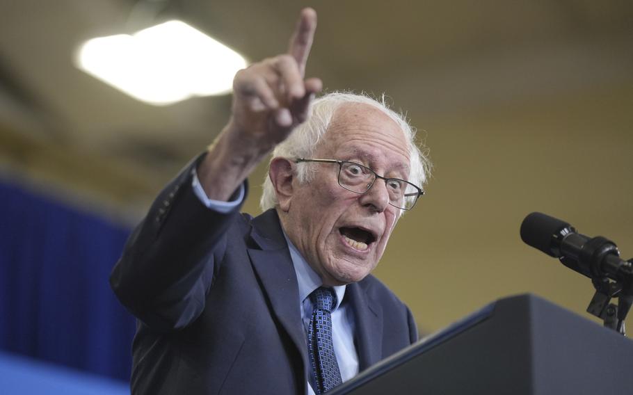 Bernie Sanders raises his hand and points while making a speech at a podium.