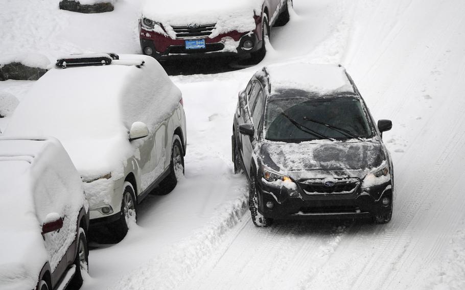 Cars along the road in Denver are covered in snow as one car, already cleared, pulls away.