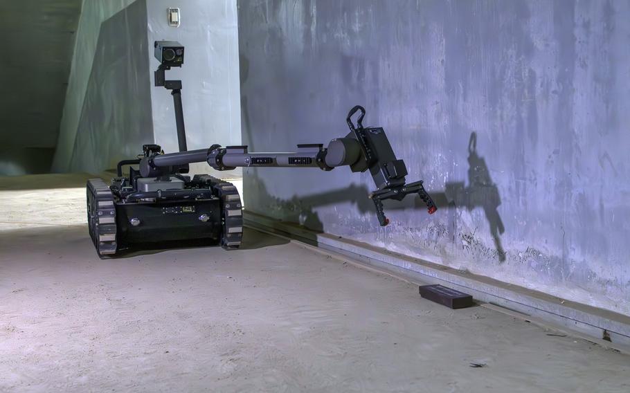 A robot with pincers on the front is used to pick up a simulated IED.