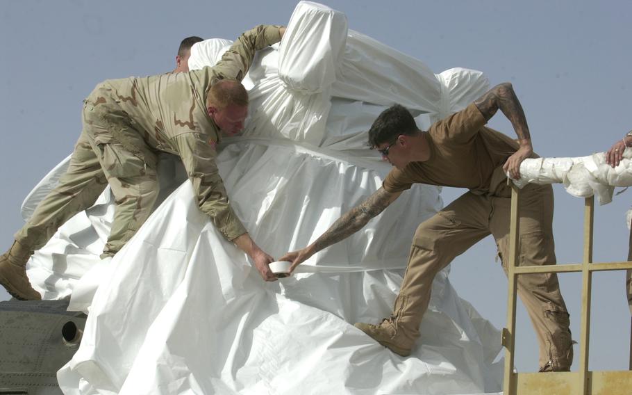 Soldiers wrap plastic around a Chinook helicopter