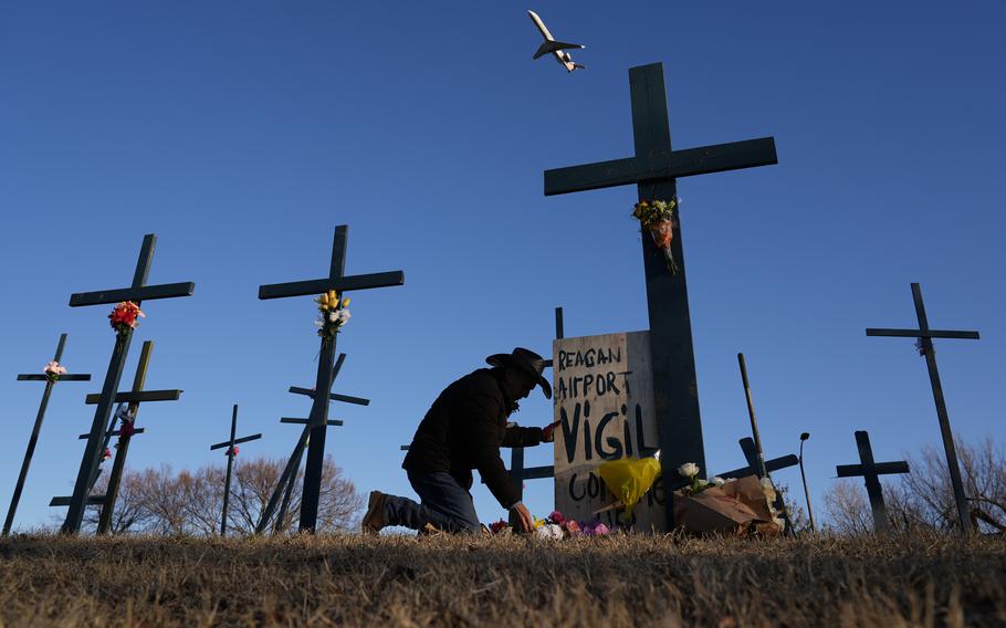 A plane flies over a memorial with crosses and flowers.