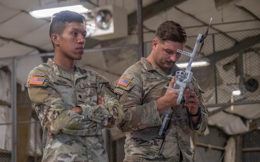 A 101st Airborne Division soldier examines a drone as another soldier stands nearby.