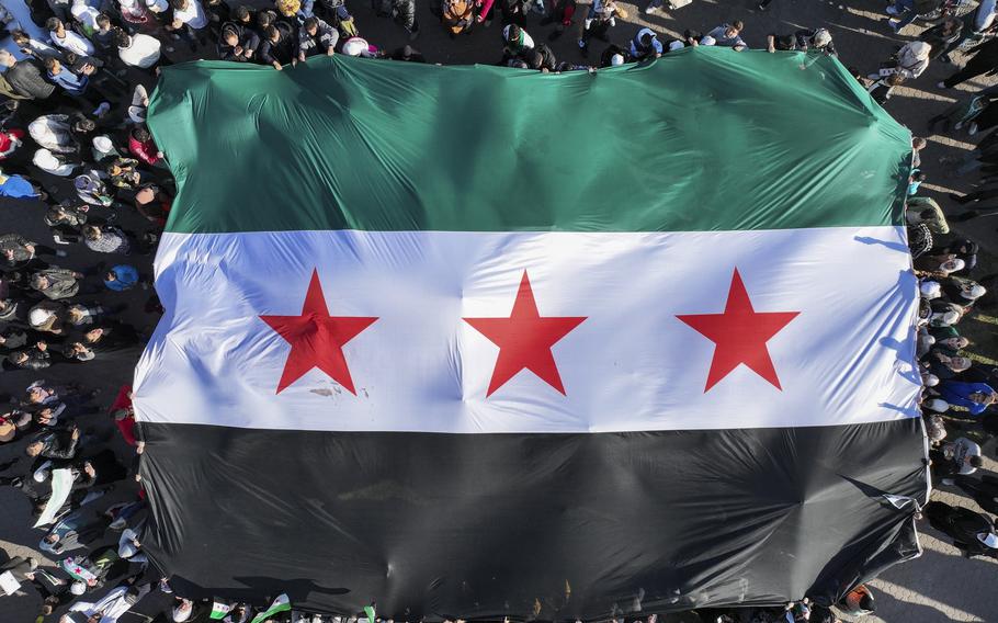 People outside hold up a large Syrian flag.