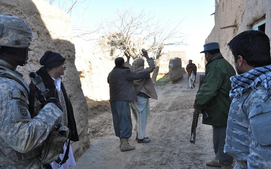 An Afghan National Police officer searches passers-by as U.S. soldiers from the 4th Squadron, 73rd Cavalry Regiment of the 82nd Airborne look on following a small bomb attack in the village of Dashta Bam in the Pashtun Zarghun district of Herat province earlier in the day. The device only partially exploded just after the last U.S. vehicle passed, causing no damage.