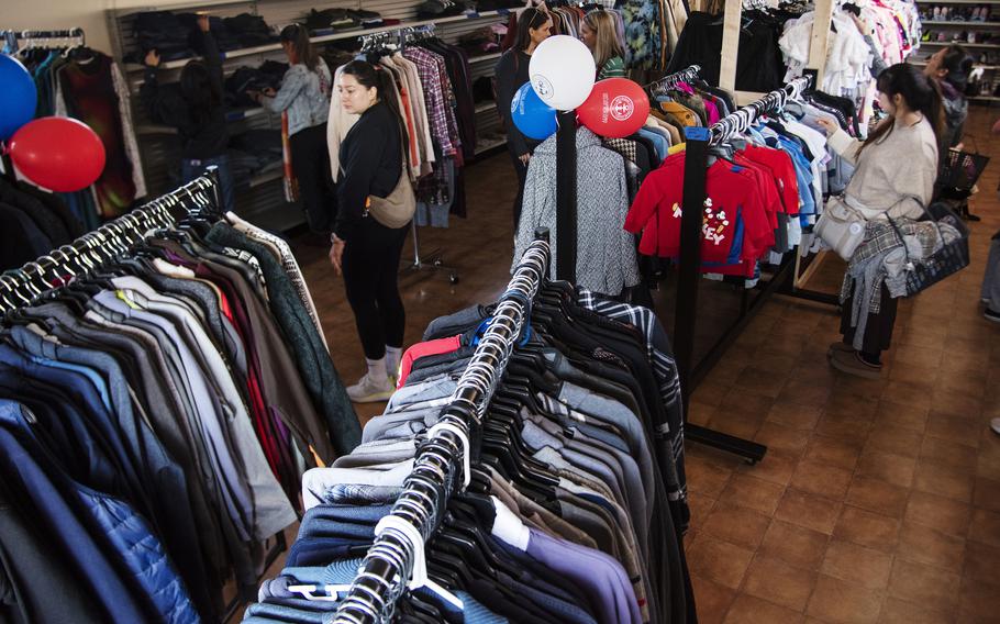 Customers browse through racks of clothing on hangers inside a retail store.