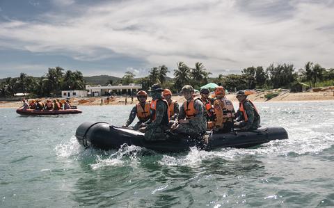 People in uniforms and wearing helmets and life vests sail in small inflatable vessels in the ocean.