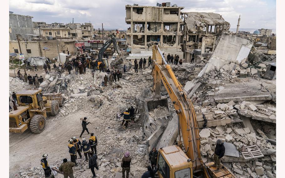 White Helmet rescue workers dig through rubble for the body of a 13-year-old boy and others on Friday, Feb. 10, 2023, after a building collapsed in the town of Jinderis, Syria. 