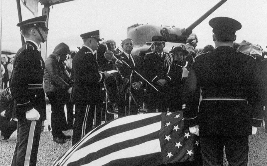 Lt. Gen. Ronald Watts, commander of VII Corps, Stuttgart, Germany, stands at a microphone Nov. 16, 1987, prior to the dedication of the memorial honoring 749 American troops killed in a rehearsal for the D-Day landings that took place in Slapton Sands, England. The memorial is in the foreground draped with the American flag.