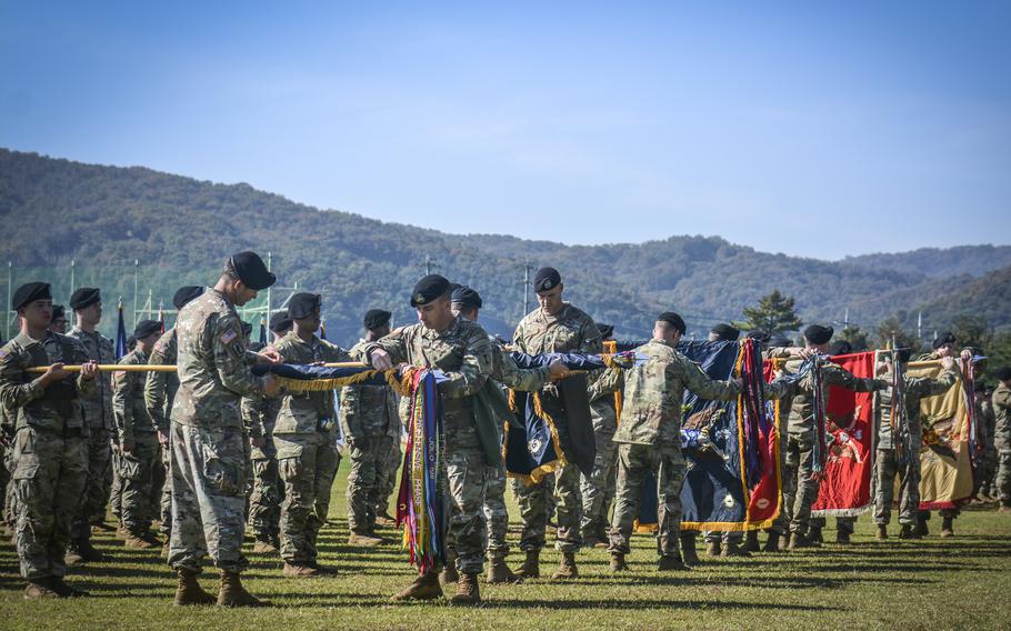 Soldiers uncase unit guidons with a blue sky and hills in the background.