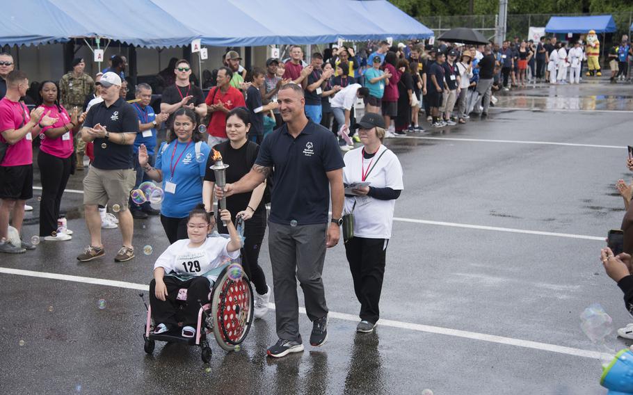 A young girl seated in a wheel chair carries the Olympic flame in a torch.