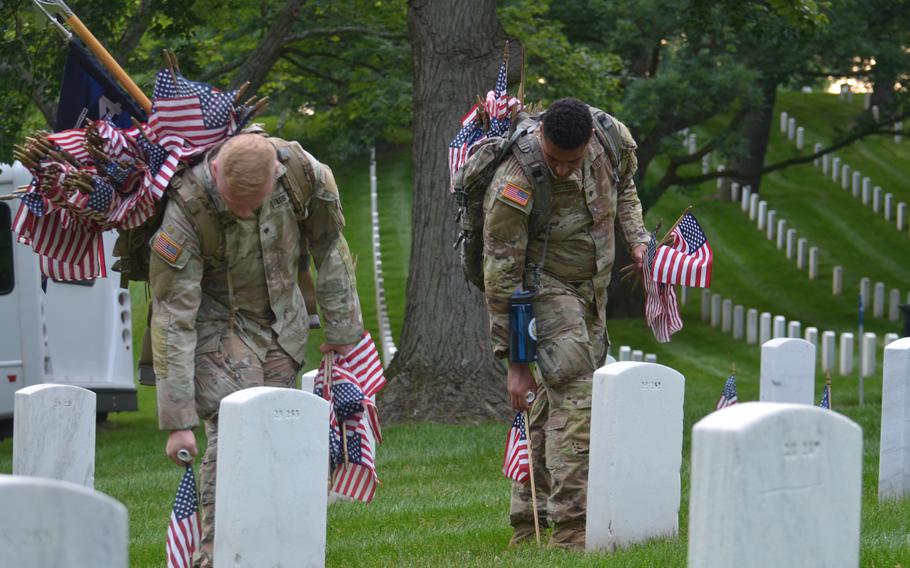 Spc. Oliver Eriksson, left, and Spc. Norman Rindfliesch place flags at the graves of those buried at Arlington National Cemetery for “Flags In” on Thursday, May 23, 2024, to honor fallen service members for Memorial Day. 