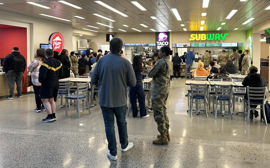 Customers stand in front of the Camp Walker food court with Subway and Pizza Hut signs in the background. 