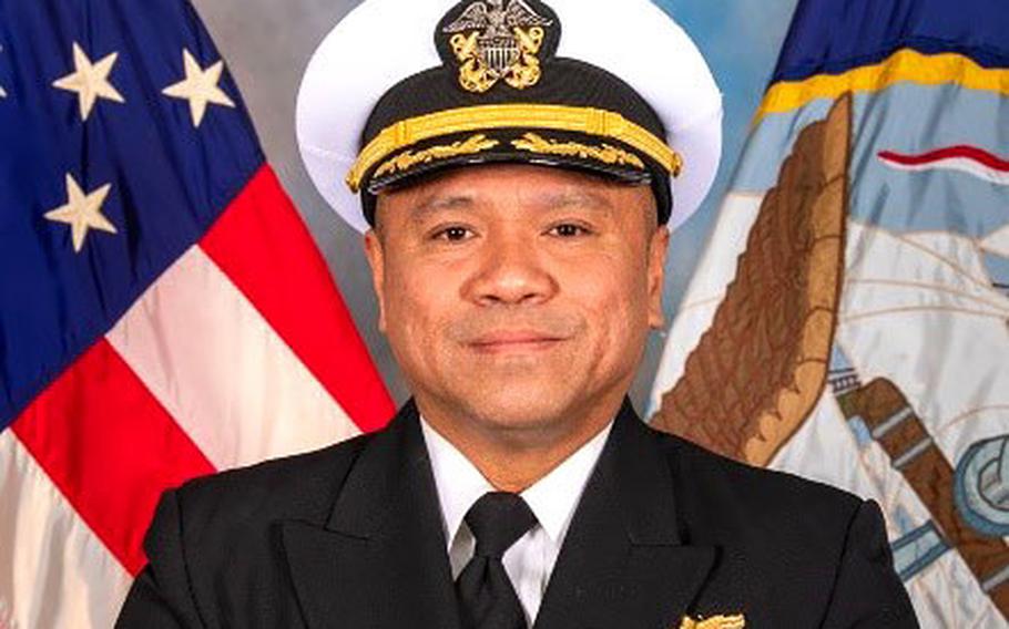 A man dressed in a Navy uniform smiles for a professional headshot.