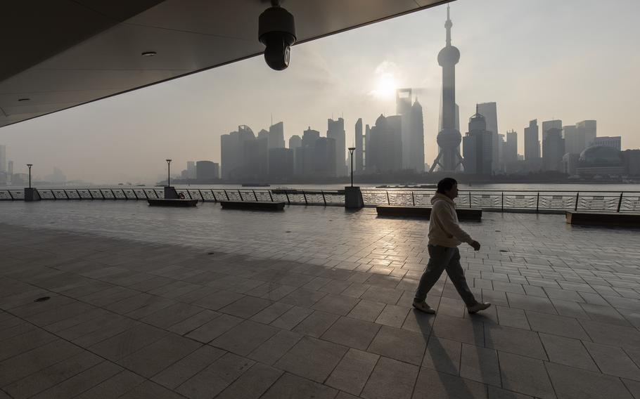 A pedestrian walks along the Bund past a surveillance camera and buildings in the Lujiazui Financial District at sunrise in Shanghai, China, on Tuesday, Jan. 4, 2022.