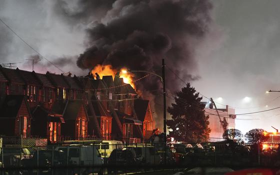 Flames and dark smoke rise into the twilight sky over a row of houses.