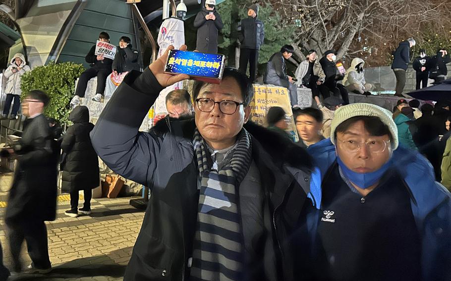 A demonstrator outside of South Korea’s National Assembly holds a phone with protest text by his forehead.