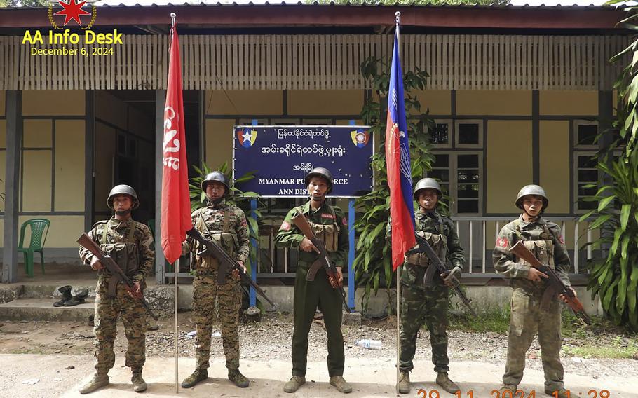 Five members of the Arakan Army stand holding rifles in front of a police building.