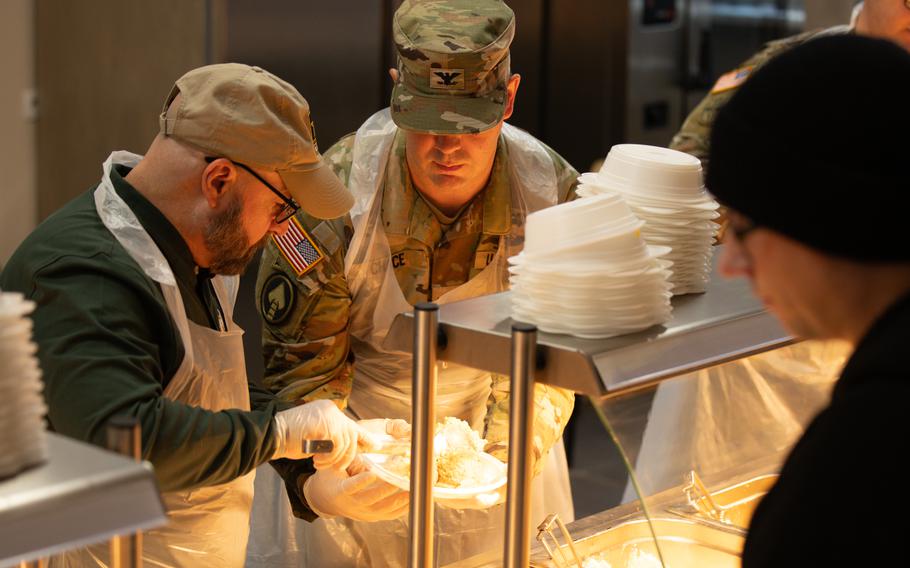 Col. Jesse Chace, USAG-Poland Commander, and Mr. Matt De Pirro, USAG-Poland Deputy Garrison Commander, serve Thanksgiving plates to service members 