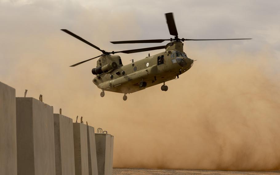 An Army Chinook helicopter kicks up dust as it lands in desert terrain.