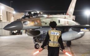 A man in a vest ground guides a small military plane.