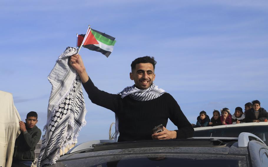 A man standing outside of a car’s sunroof waves a Palestinian flag and kufiyah.