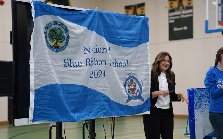 The DODEA Europe director for student excellent stands and smiles next to a Blue Ribbon flag.