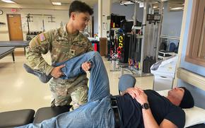 Then-Spc. Joelle Pamplona holding the raised leg of a patient lying on a bed, in October 2023.