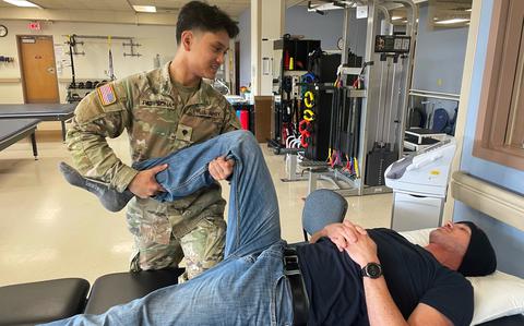 Then-Spc. Joelle Pamplona holding the raised leg of a patient lying on a bed, in October 2023.