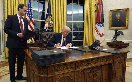 President Donald Trump signs an executive order at his desk in the Oval Office.