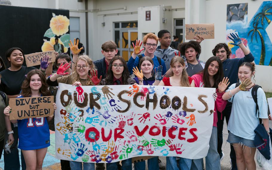 Students pose with signs reading, “Diverse but United,” “Diversity is not a threat,” and “My Voice Matters” as well as a banner that says,“Our Schools, Our Voices.”