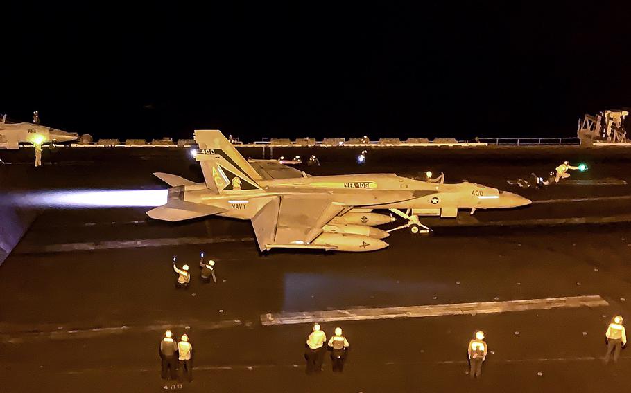 A fighter jet, with flight crew members on the deck, begins its launch.