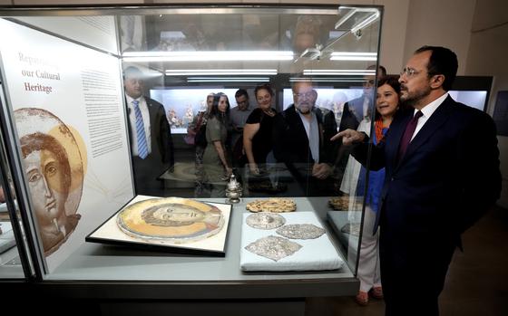 Cyprus' President Nikos Christodoulides, right, stands in front of an Orthodox Christian icon after the same was repatriated and displayed at the Archeological museum in capital Nicosia, Cyprus, Monday, July 22, 2024. The returned artifacts numbering around 60, including jewelry from the Chalcolithic Period dating between 3500-1500 BC, Bronze Age bird-shaped idols, jars and spearheads as well as many Orthodox Christian icons were part of a larger haul of 250 antiquities that German authorities had seized from Turkish art dealer Aydin Dikmen in 1997. 