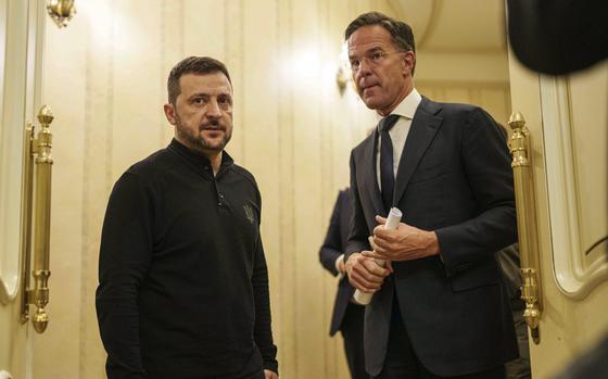 NATO Secretary General Mark Rutte and Ukrainian President Volodymyr Zelenskyy stand in a hallway and speak with one another.