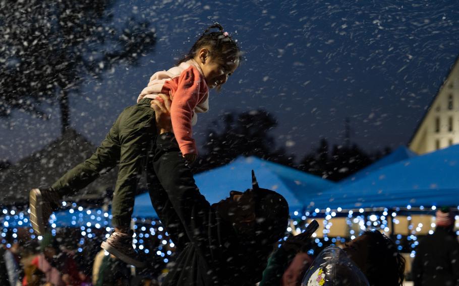 A man holds a child up smiling child up with lights all around.