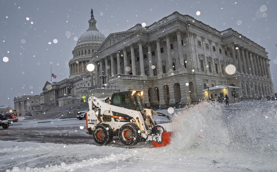 A snowplow can be seen shoveling snow in front of the US Capitol building.