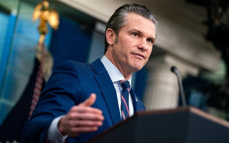 Defense Secretary Pete Hegseth, seen from a low angle, stands at a podium and speaks into a microphone.