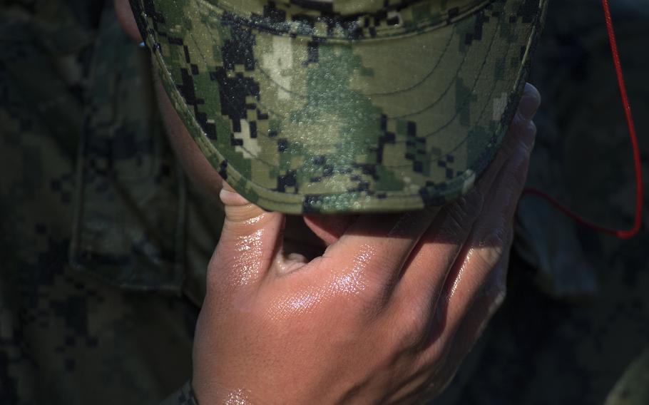 A SEAL holds his hand to his face under the brim of his hat during training.