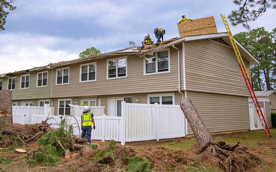 Construction workers on the roof of a house repair the damaged roof.