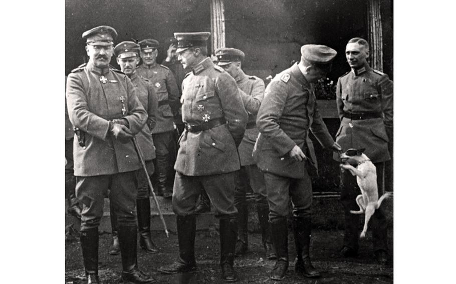 A small white dog jumps next to a group of service members.