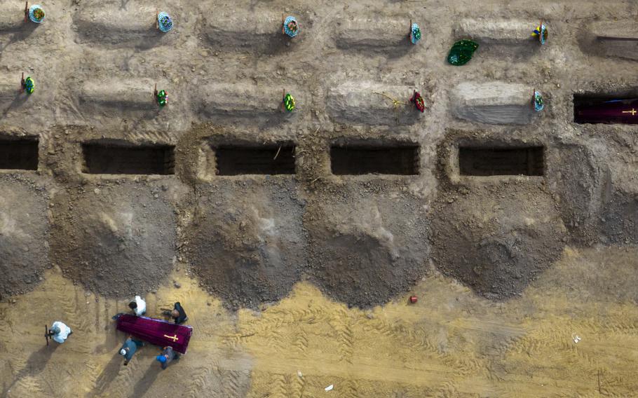 People carry a casket to one of many open graves in a line.