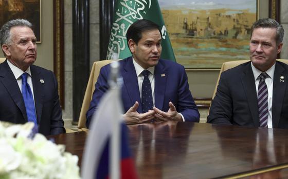 Secretary of State Marco Rubio sitting between two other men in suits at the corner of a table.